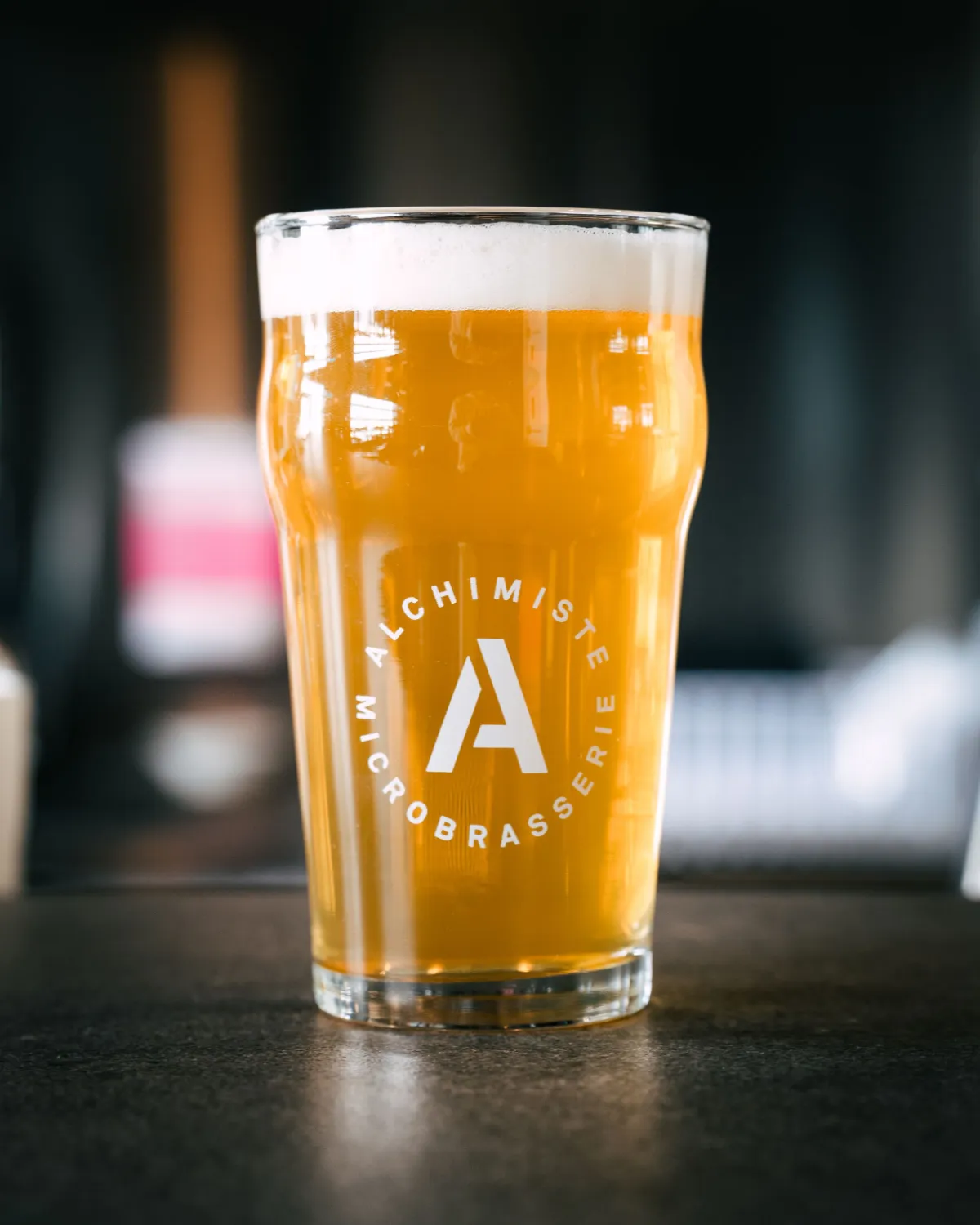 Verre de bière L’Alchimiste sur fond sombre